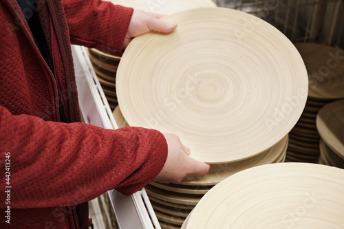 Woman in a store buys a large, round wooden plate made of natural wood. The concept of buying new dishes and kitchen equipment. Hands close up shot