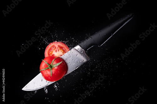 Fresh ripe tomato cutting with a knife and flying in motion on the black background with red splashes photo