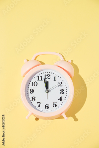 The alarm clock in pink on a yellow background displays 5 minutes to 12