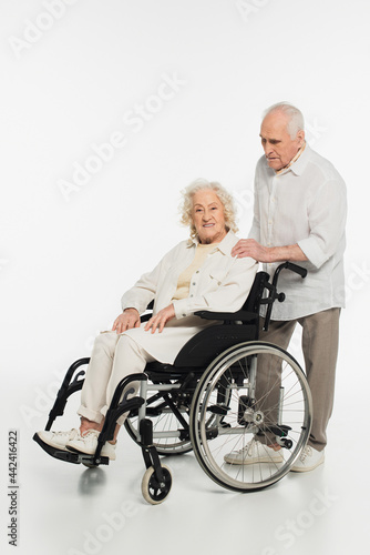 elderly man holding hand on shoulder of wife in wheelchair isolated on white © LIGHTFIELD STUDIOS
