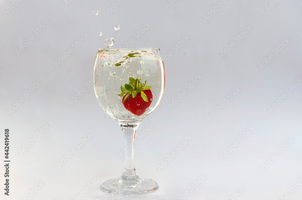 Obraz premium Summer.Bar. Cocktails. Drinks. Strawberries are immersed in a clear liquid in a glass on a high stem. Splashes and drops hung in the air.White background.A wine glass.A clear silhouette of a red berry