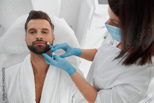 Happy man with beard undergoes nasolabial fold filler procedure in cosmetology clinic
