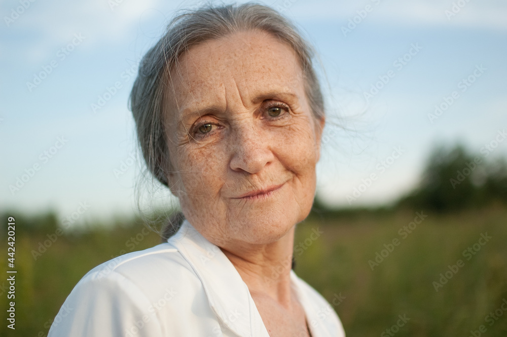 Portrait of senior woman with grey hair and face with wrinkles wearing white jacket and relaxing at park during sunny day Portrait of senior woman with grey hair and face with wrinkles wearing white jacket and relaxing at park during sunny day