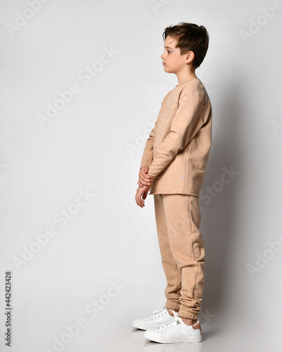 Serious thoughtful confident preteen boy child in fashion sportswear thinking looking forward on copy space standing . sideway over studio wall background. Children emotion and expression concept