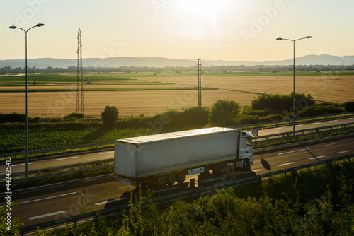 White Truck with semi-trailer driving along highway on the sunset sky and rural background. Services and Transport logistics photo