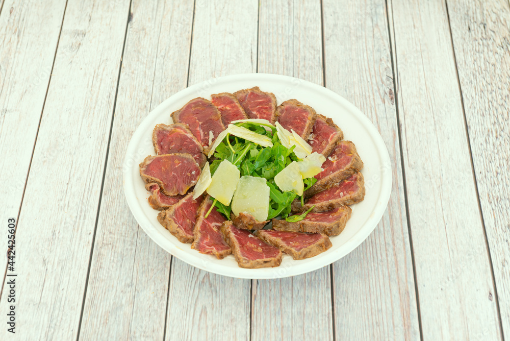 Beef tataki with parmesan cheese flakes and a little arugula with oil and salt in a plate for home delivery