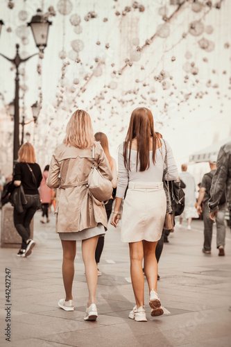 Unrecognizable girls walking on city street, view from behind. Modern lifestyle. Regular people out in public places