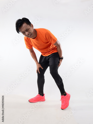Male Asian runner having rear leg pain, hamstring muscle cramp because of not doing warm up before run exercise. High key studio shot, sport injury