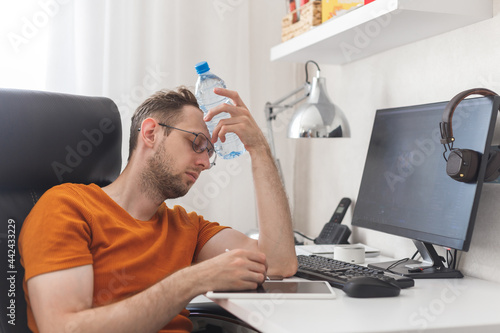Working at home man suffering from heat and thirst cools down with water bottle at hot summer day