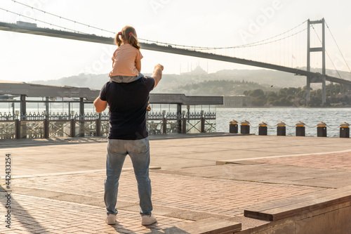 Photography Little cute girl seat on father's shoulders in front of Bosphorus bridge (aka: 15 July Martyrs Bridge Turkish: 15 Temmuz Sehitler Koprusu) in Ortakoy, Istanbul, Turkey