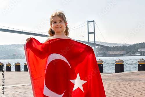 Girl hold Turkish flag near Bosphorus bridge (aka15 July Martyrs Bridge or 15 Temmuz Sehitler Koprusu) in Ortakoy, Istanbul, Turkey. Patriotism. Turkish National Sovereignty and and Children's day.