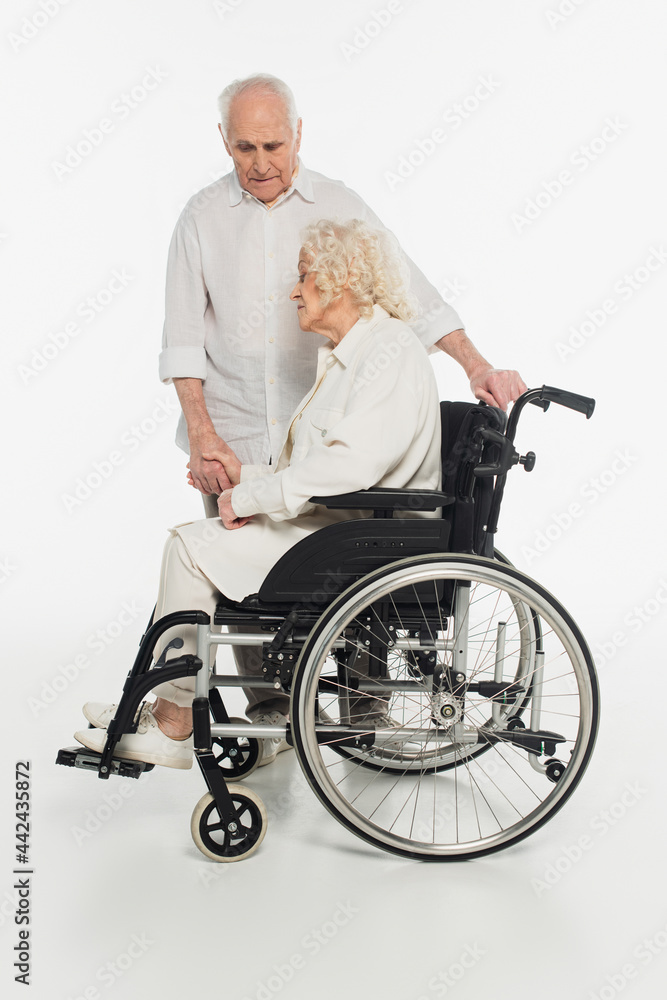 sad elderly woman in wheelchair holding hand of husband on white sad elderly woman in wheelchair holding hand of husband on white