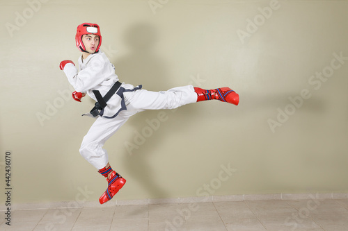 Taekwondo fighter doing a flying back kick, dressed in white uniform and black belt. With red protective elements.