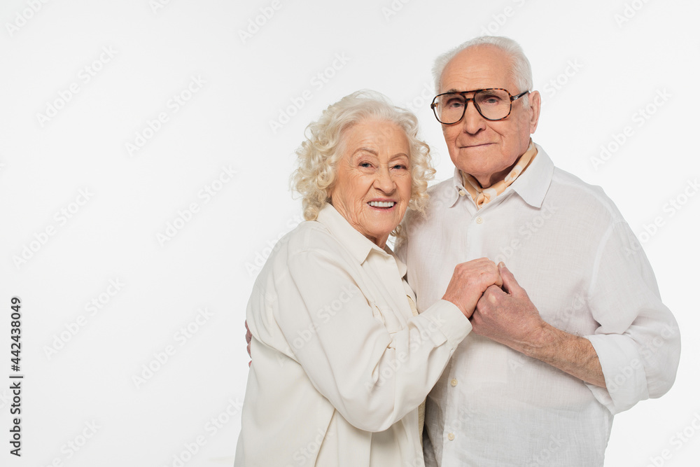 elderly couple in casual clothes hugging with holding hands and looking at camera isolated on white elderly couple in casual clothes hugging with holding hands and looking at camera isolated on white