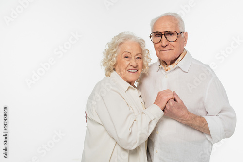 elderly couple in casual clothes hugging with holding hands and looking at camera isolated on white