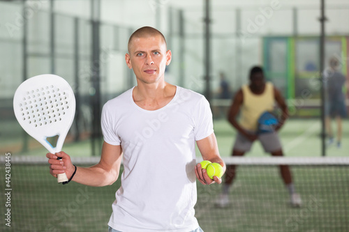 Positive adult sportsman looking at camera while playing padel at court indoor © JackF