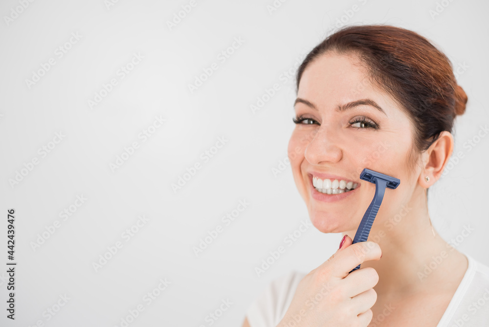 Caucasian smiling woman shaves face with razor on white background. Empty space. Caucasian smiling woman shaves face with razor on white background. Empty space.