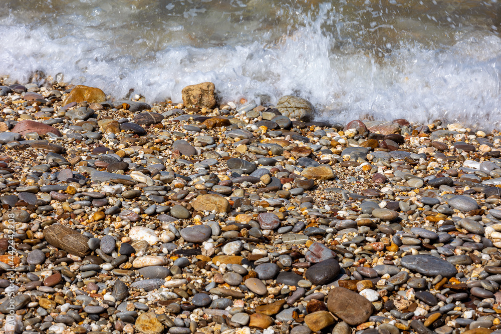 Top view of sea rocks or granite pebbles while getting light waves making white bubbles and light reflection. Background of wet stone at sea shore Top view of sea rocks or granite pebbles while getting light waves making white bubbles and light reflection. Background of wet stone at sea shore