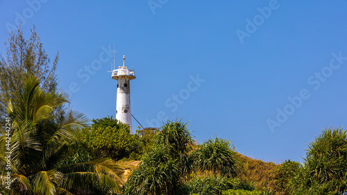 White lighthouse tower on the top of greenery forest with clear blue sky background on sunny day