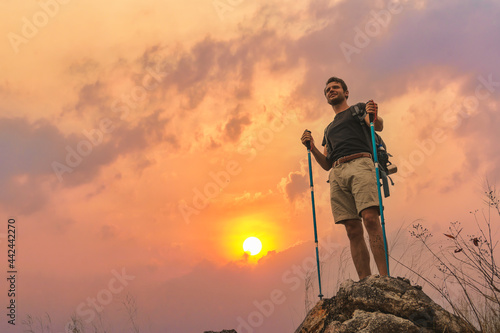 hiker with trekking stick hiking success on rocky hill top at sunset sky