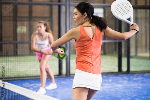 Young sporty kazakh woman padel player hitting ball with a racket on a hard court