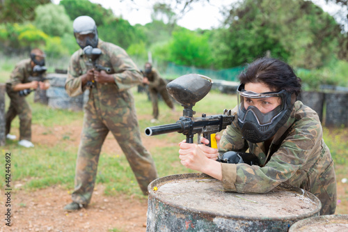 Portrait of girl paintball player in mask who is aiming in opponents on paintball field