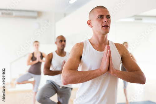 Focused man exercising yoga with group of young adult sporty people in studio