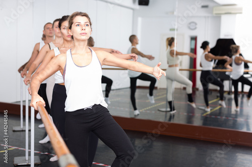 Group of people doing exercises using barre in gym with focus to fit athletic toned .woman in foreground in health and fitness concept.