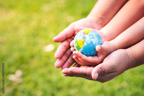 Fototapeta Naklejka Na Ścianę i Meble -  World environment day concept.  A mother's hand embrace her little daughter's hands. Child hand's who is holding carry the world. Blurred green lawn background. Protect our globe. Copy space.