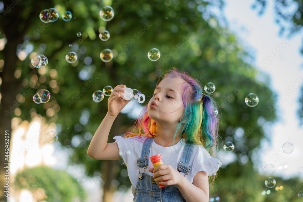 caucasian little girl is blowing a soap bubbles in park. Image with selective focus