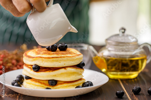 Selcetive focus on Strawberry jam pouring on pancake with blueberry fruit in white plate on teapot background. photo