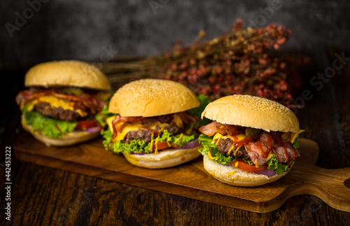 Three hamburgers with beef burgers, fried onions, spinach, ketchup, pepper and cheese served on a wooden board floor with soft drink.