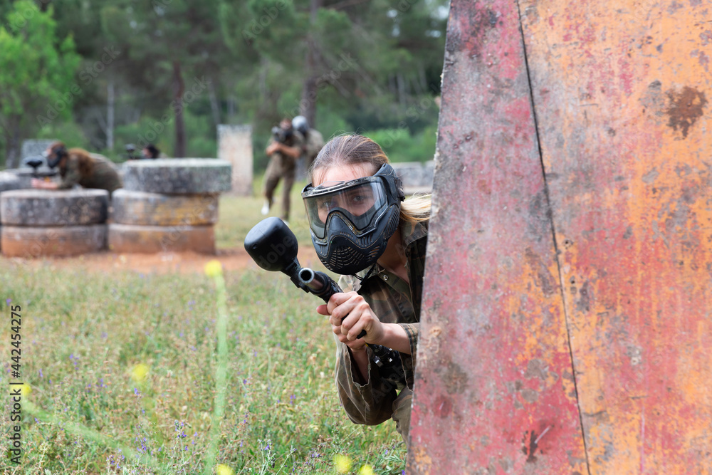 Fototapeta premium Portrait of girl paintball player in mask who is aiming in opponents on paintball field