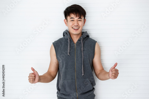 Asian handsome fit smiling man holding hand thumbs up show great wearing sleeveless t-shirt gray sportswear in white background.
