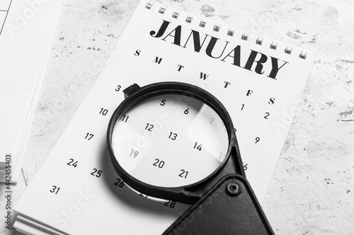 Flip paper calendar and magnifier on light background, closeup