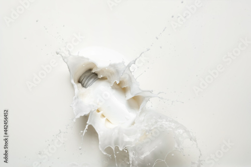 Bottle of cosmetic product falling into splashing milk photo