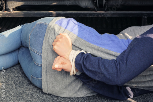 Female hostage with tied hands lying inside car, closeup photo