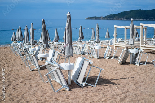 Empty white sun loungers without people under umbrellason the pebble beach by the sea. © ukrolenochka