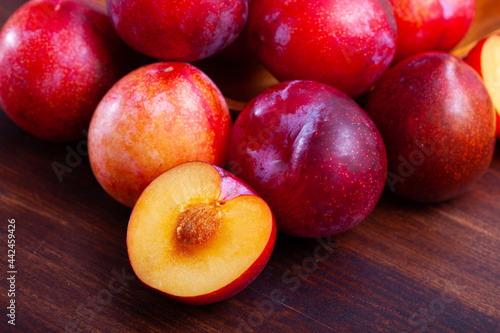 Cuadro en lienzo Whole and halves red appetizing plums on wooden table