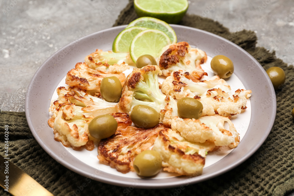 Plate with tasty fried cauliflower, lime and olives on grunge background Plate with tasty fried cauliflower, lime and olives on grunge background