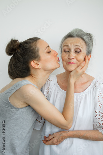 Happy senior mother is hugging her adult daughter, the women are laughing together, sincere family of different age generations having fun on white background