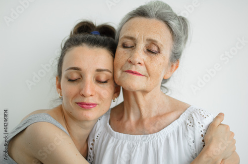 Happy senior mother is hugging her adult daughter, the women are laughing together, sincere family of different age generations having fun on white background