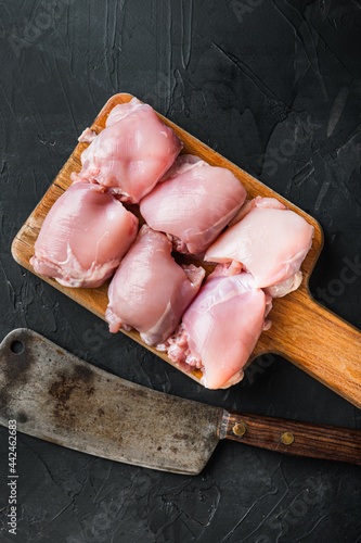 Raw chicken thighs with meat cleaver, on black background, top view