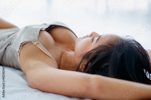 Beautiful young naughty girl with sexy pajamas seductively lie down on bed with ease and close her eyes to relax in bright tranquil morning of rest day