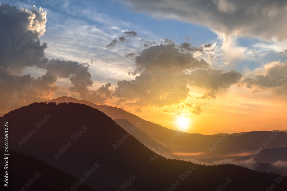 Sunset landscape of high mountain peaks and foggy valley under vibrant colorful evening sky.