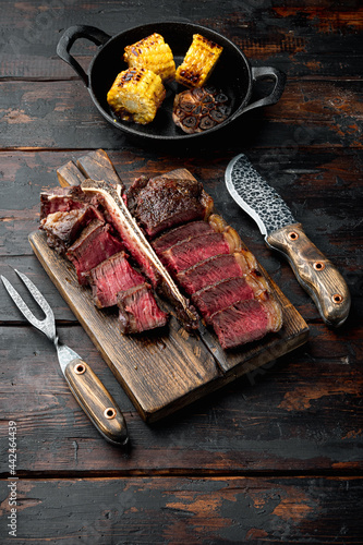 Medium rare dry aged beef steak grilled and sliced, t bone or porterhouse cut, on wooden serving board, on old dark  wooden table background, with copy space for text