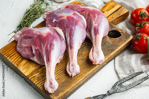 Raw goose legs thighs , with herbs and ingredients, on wooden cutting board, on white stone  background