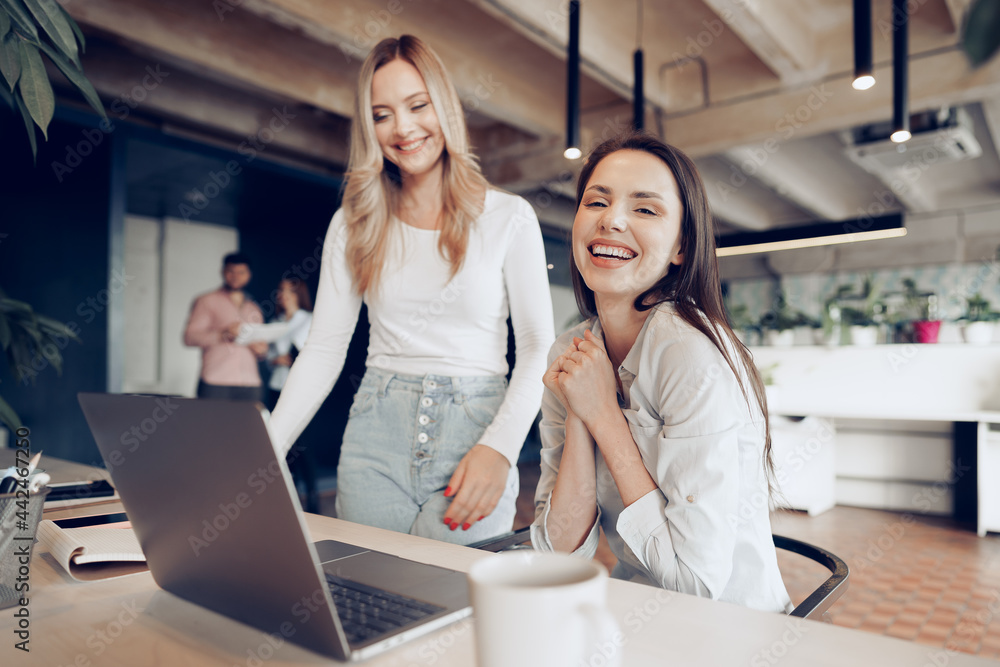 Two young happy businesswomen celebrating project success in office Two young happy businesswomen celebrating project success in office