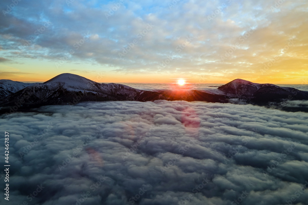 Aerial view of vibrant sunrise over white dense fog with distant dark Carpathian mountains on horizon. Aerial view of vibrant sunrise over white dense fog with distant dark Carpathian mountains on horizon.
