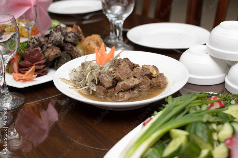 Slices of delicious stewed lamb meat with onions and gravy on a white plate on the banquet table Slices of delicious stewed lamb meat with onions and gravy on a white plate on the banquet table